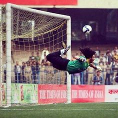 a soccer goalie jumps to catch the ball in mid air as spectators watch from the sidelines