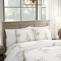 a bed with white sheets and pillows in front of a window next to a lamp