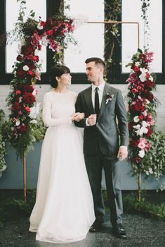 a man and woman standing next to each other in front of a wall with flowers