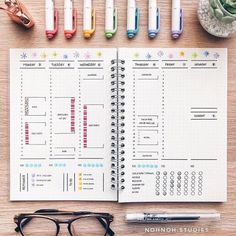 an open planner sitting on top of a wooden table next to pens and glasses,