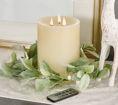 a lit candle sitting on top of a table next to a remote control and greenery