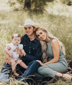 a man and woman are sitting in the grass with a baby