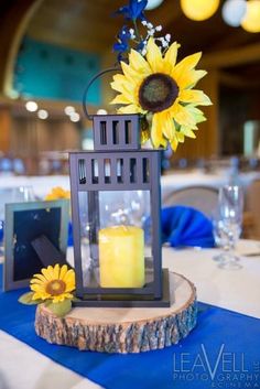 a table topped with a vase filled with sunflowers and a lit candle on top of a piece of wood