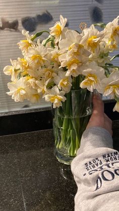 a person's hand reaching into a vase filled with yellow and white flowers