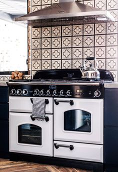 an old fashioned stove and oven in a room with wood floors, patterned wallpaper