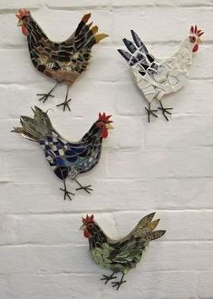 four metal roosters are hanging on a white brick wall, each with different designs and colors