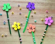 three flowers made out of plastic beads on a wooden surface with numbers pinned to them