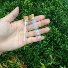 two small glass tubes sitting in the palm of someone's hand with green plants behind them