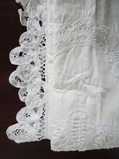 two pieces of white linen with lace on them sitting next to each other in front of a wooden table