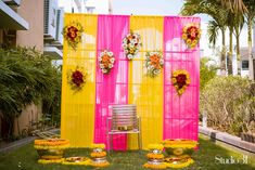 an outdoor ceremony setup with yellow and pink draping, flowers on the back wall