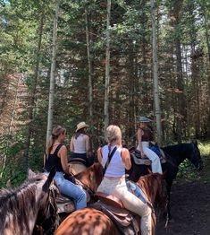 three women are riding horses in the woods