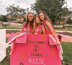 three girls are posing in front of a pink sign that says welcome to the team