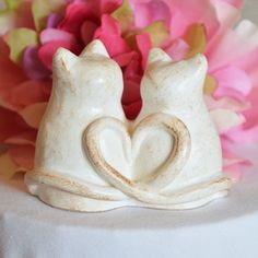 two ceramic cats sitting next to each other on a table with flowers in the background