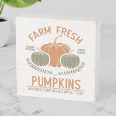 a wooden sign with pumpkins on it sitting next to a potted plant