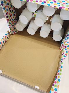 there are many white cups in the box on the table with polka dot paper around it