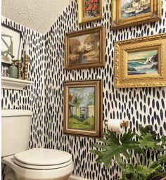 a white toilet sitting in a bathroom next to a potted plant and pictures on the wall