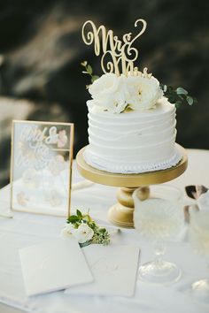 a white wedding cake sitting on top of a table next to a couple's initials