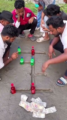 several men are playing a game with bottles and money on the ground in front of them