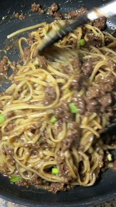 someone stir frys noodles with meat in a skillet