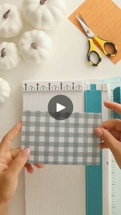 two hands holding a piece of paper next to scissors and other crafting supplies on a table