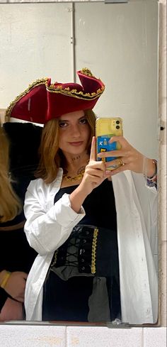 a woman taking a selfie in front of a mirror wearing a pirate hat and holding a cell phone