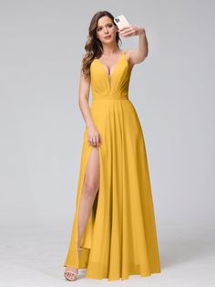 a woman in a long yellow dress posing with her leg up and holding a cell phone