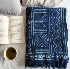 an open book sitting on top of a bed next to a cup