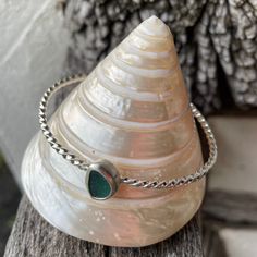 a silver bracelet with a green stone on it sitting on top of a wooden table