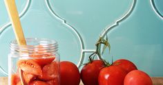 tomatoes in a jar with a wooden spoon next to them on a cutting board against a blue tile wall