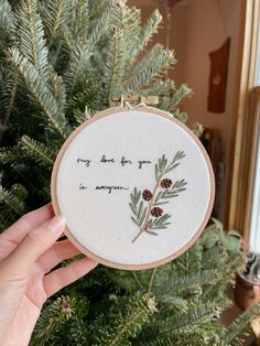 someone is holding up a hand embroidered christmas ornament with pine cones on it