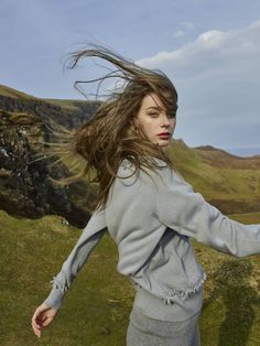 a woman with her hair in the wind on a grassy hill side, looking at the camera