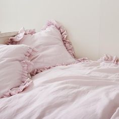 a bed with pink ruffled pillows and white sheets on top of it's headboard