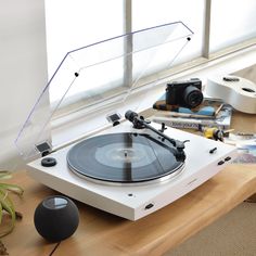 a record player sitting on top of a wooden table next to a window with a camera