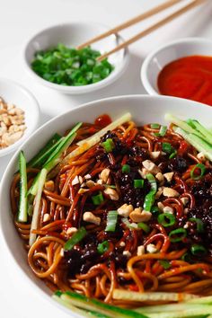 a bowl filled with noodles and vegetables next to bowls of dipping sauces on the side