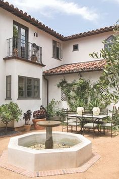 a fountain in front of a white building with tables and chairs around the outside area