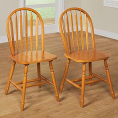 two wooden chairs sitting on top of a hard wood floor next to an open window