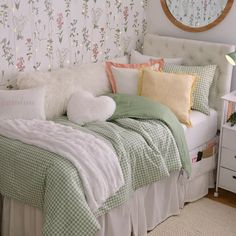 a bed with green and white comforters, pillows and blankets on top of it