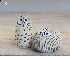 two ceramic owls sitting next to each other on top of a wooden table and one is painted white with black dots