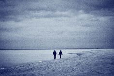 two people are walking on the beach in black and white, with dark clouds overhead