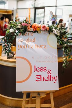 a sign with flowers on it sitting in front of a counter at a wedding reception