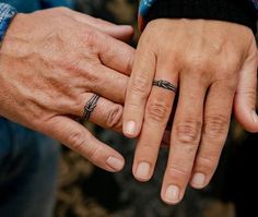 two people holding hands with wedding rings on their fingers and the other hand has an arrow tattoo on it