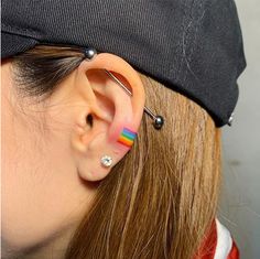 a woman wearing ear piercings with rainbow stripes on it's ears and behind her ear is a black cap