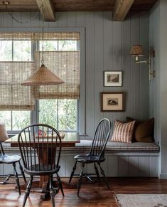 a table and chairs in a room with wood flooring, two windows and wooden blinds