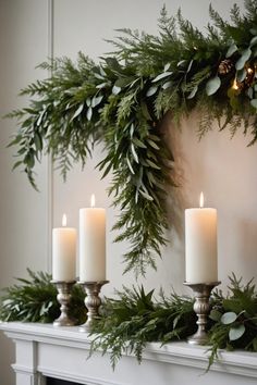 three candles are sitting on a mantle with greenery