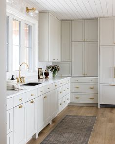 a kitchen with white cabinets and gold pulls on the handles, along with an area rug