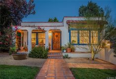 a white house with blue shutters and flowers in the front yard at night time