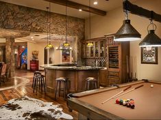 a pool table and some stools in a room with stone walls, wood flooring and an island