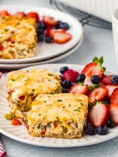 two white plates topped with food next to strawberries and blueberries on a table