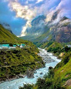 a river flowing through a lush green valley under a cloudy sky with mountains in the background