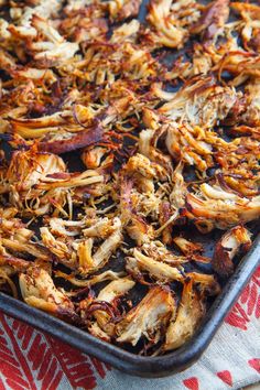 a pan filled with cooked food on top of a red and white table cloth next to a wooden spoon